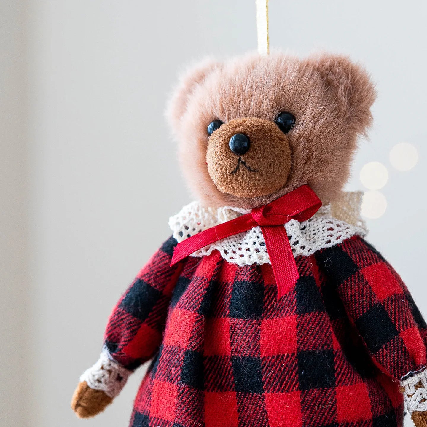 Teddy bear wearing a red and black checkered dress with a white collar against a blurred background