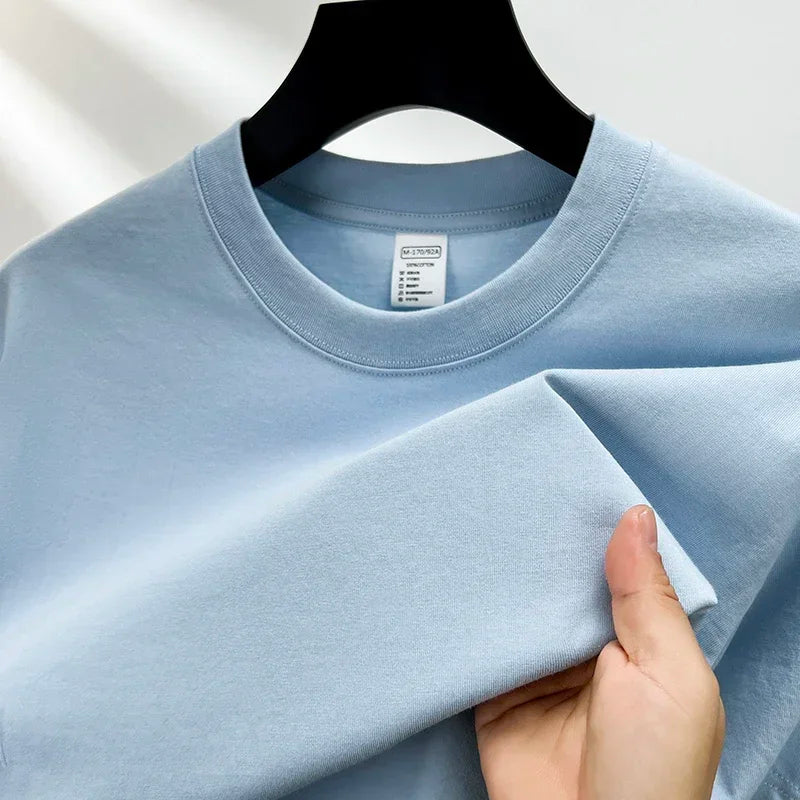 Light blue t-shirt held by a hand on a plain background