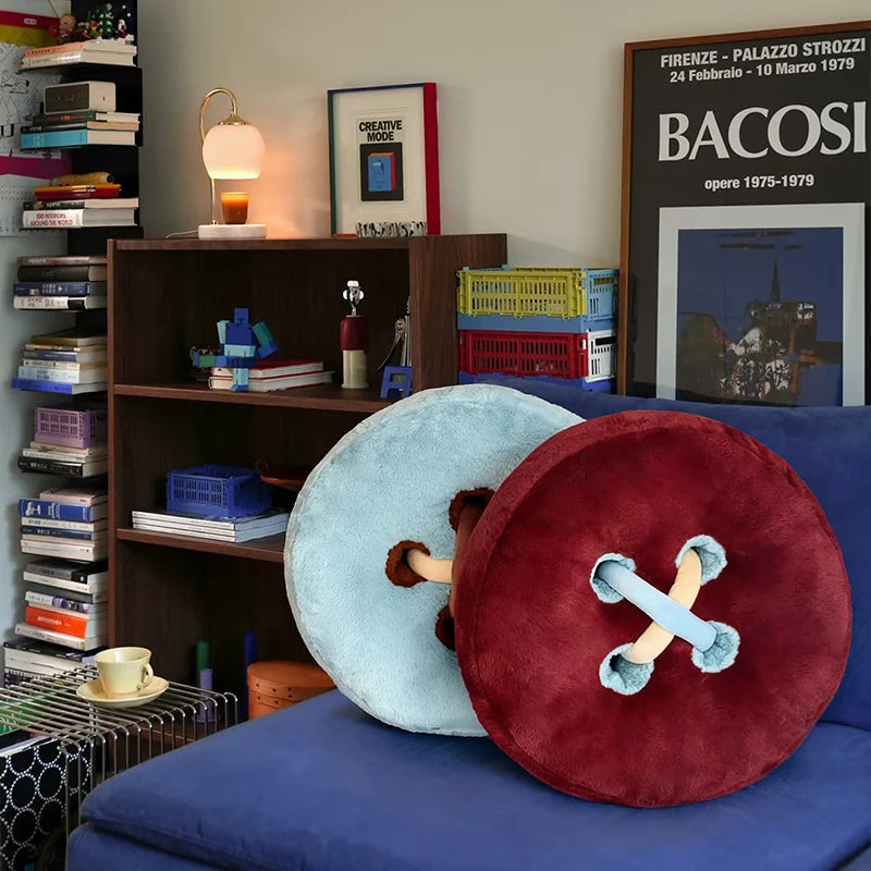 Two large decorative button cushions on a blue couch with a bookshelf and framed pictures in the background.