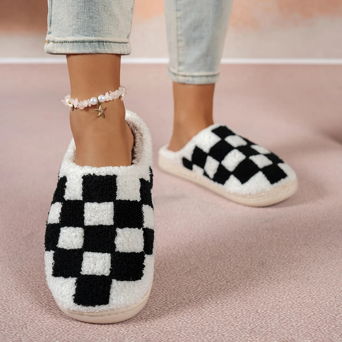 Black and white checkered slippers worn with light blue jeans on a pink background