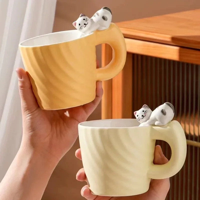 Two yellow mugs with cat-shaped handles held by a hand, placed on a wooden surface.