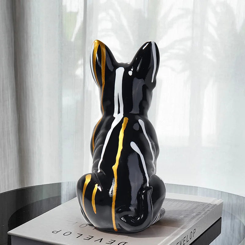 Black ceramic dog sculpture with yellow and white accents on a book against a white curtain background