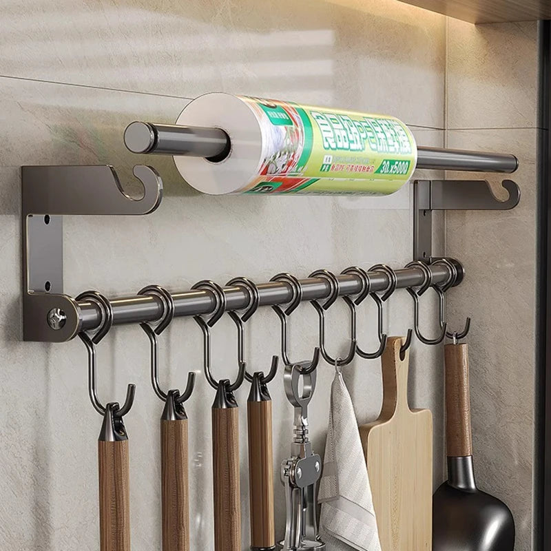 Wall-mounted kitchen rack with hooks holding utensils and a roll of paper towels.
