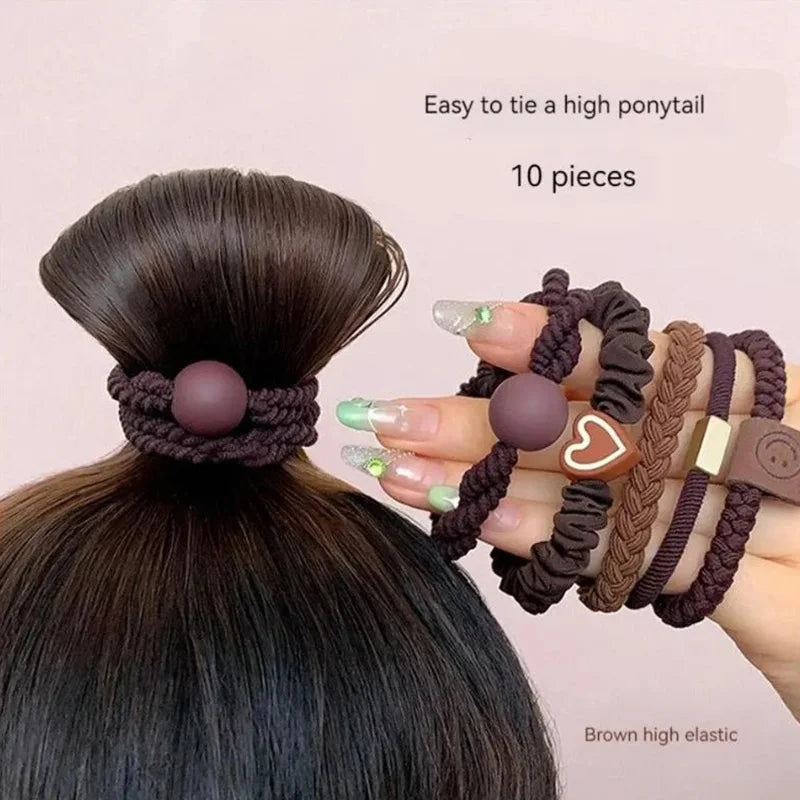 Brown hair ties with decorative elements held by a hand, worn in a high ponytail on a light pink background.