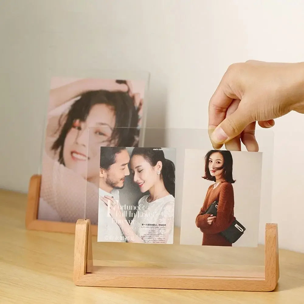 Hand holding a photo of a couple with a wooden photo stand displaying other photos on a light surface.