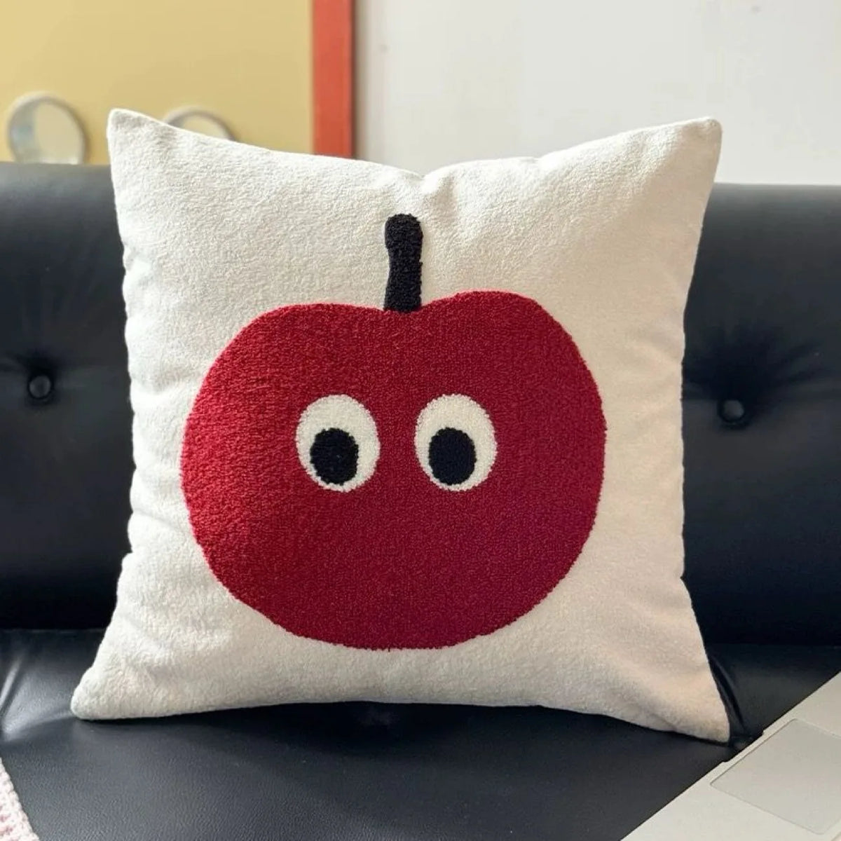 Decorative pillow with a red apple design on a black leather couch.