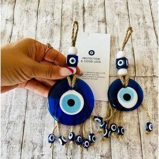 Blue evil eye glass wall hanging with rope and beads symbolising protection and good luck.