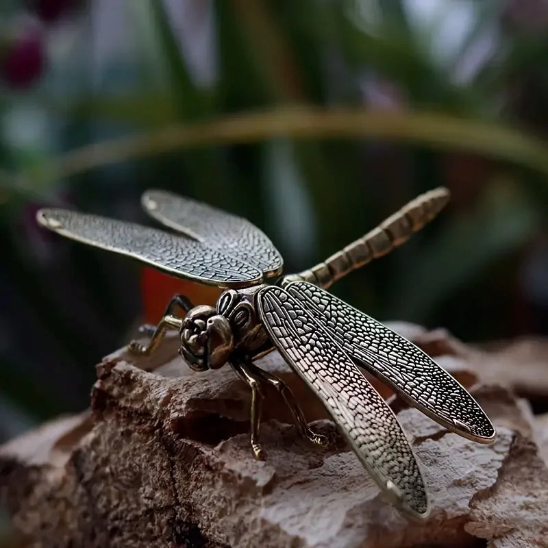Bronze dragonfly figurine on a textured surface with blurred greenery in the background