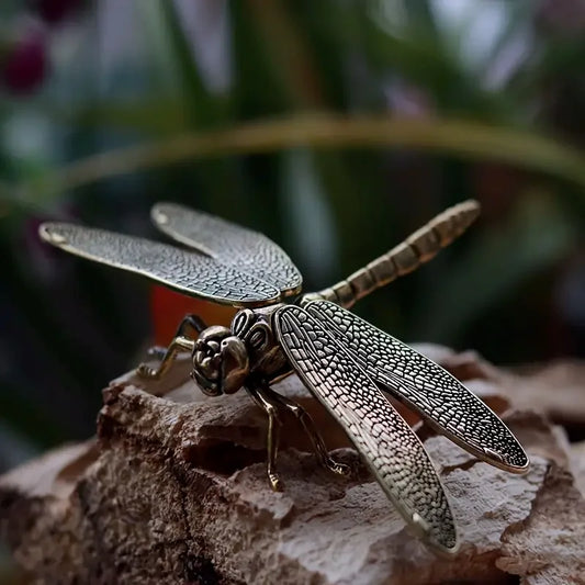 Bronze dragonfly figurine on a textured surface with blurred greenery in the background