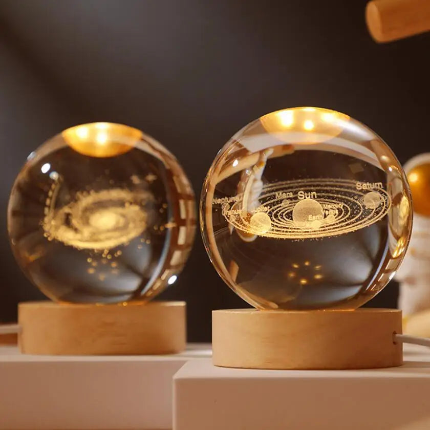 Two crystal ball night lights with engraved solar system design on wooden bases.