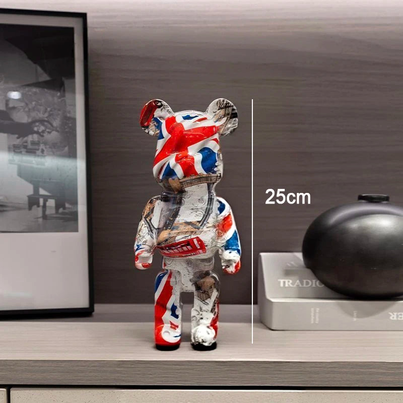 A bear-shaped collectible figure with a distressed Union Jack flag print in red, white, and blue, standing on a shelf next to a framed print and a black decorative object. A vertical measurement line and the text '25cm' indicate height.