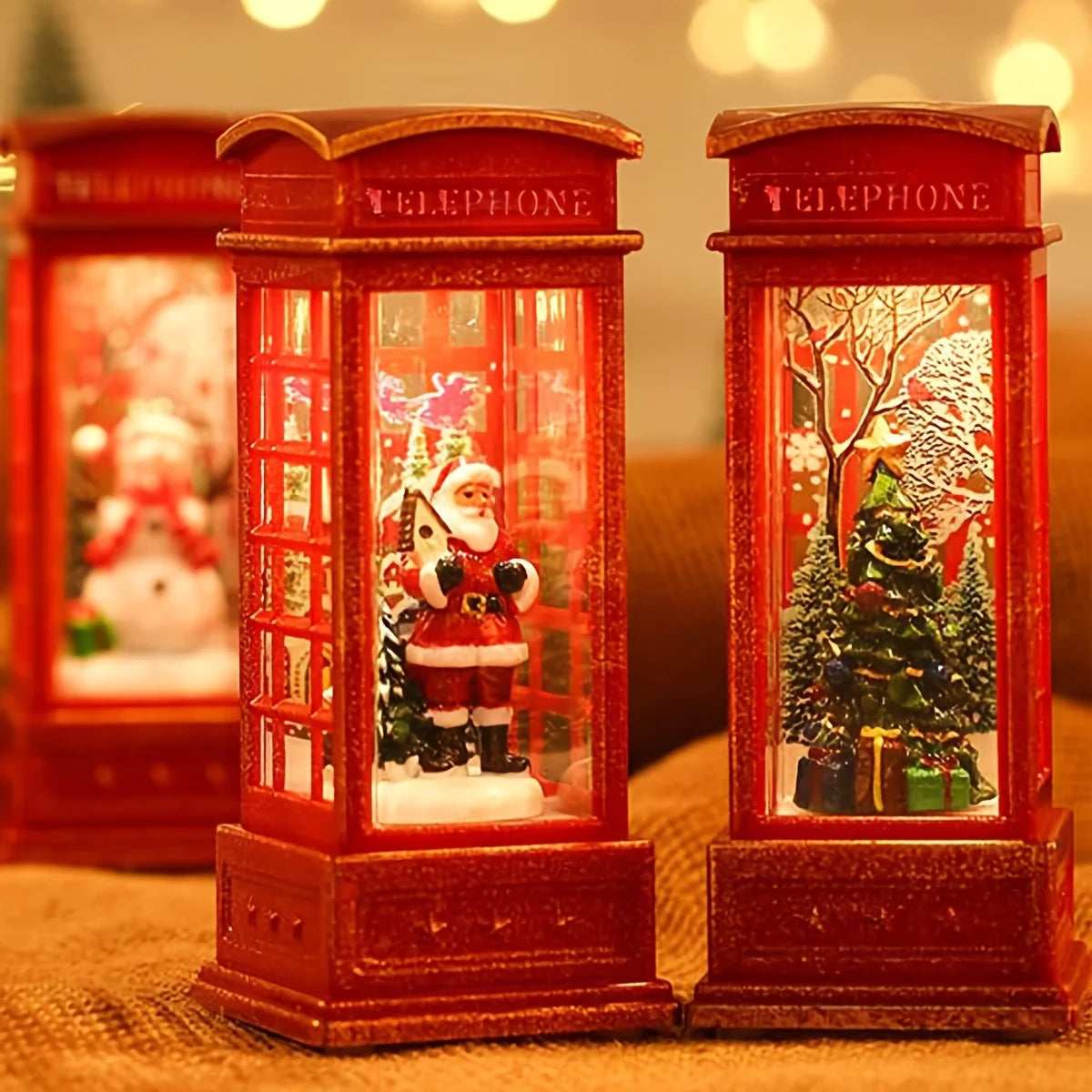 Two red telephone booth snow globes with Santa Claus and Christmas trees inside, on a blurred background.