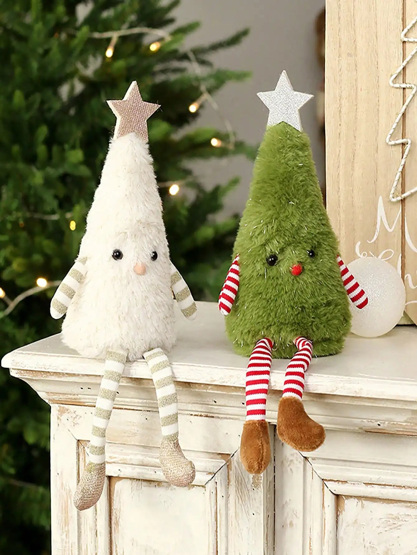 Two Christmas-themed figurines, one white and one green, on a mantelpiece with a decorated tree in the background.