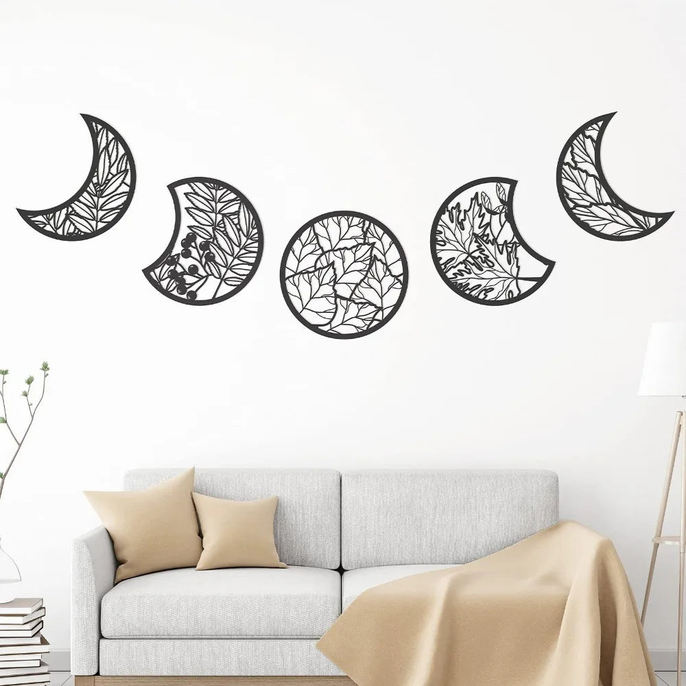 Decorative wall art of moon phases with leaf patterns on a white wall above a sofa.