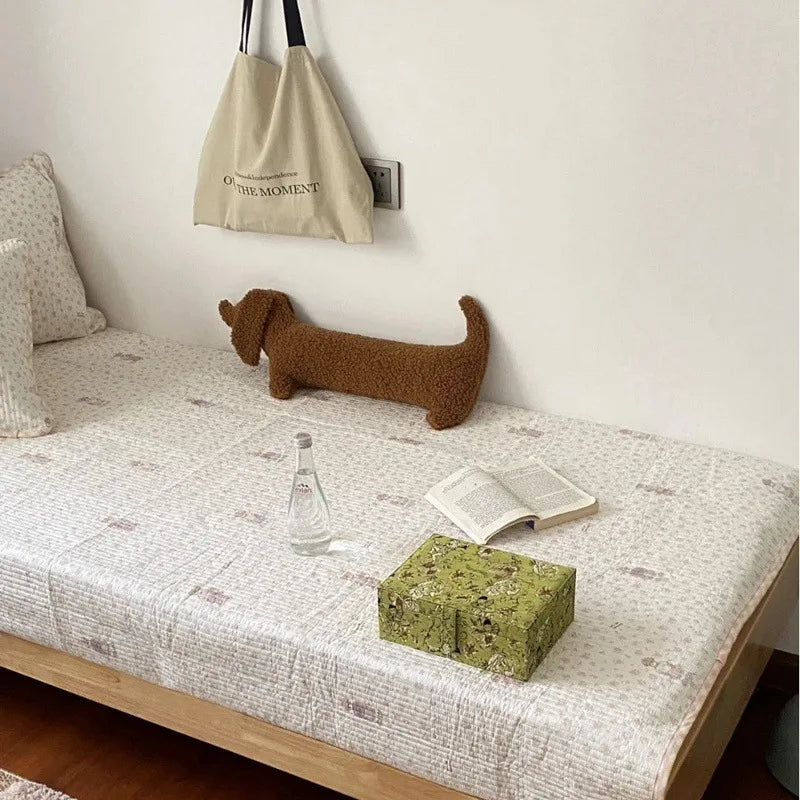 dachshund-shaped cushion on a bed with plain sheets