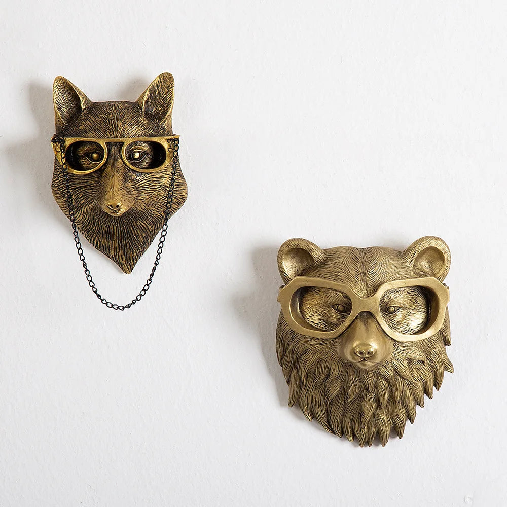 Two brass animal head wall decorations with glasses on a white background