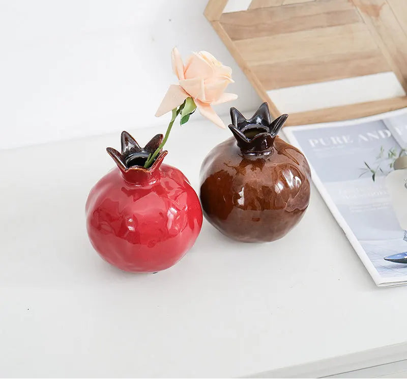Two decorative pomegranate-shaped vases with floral elements on a white surface.