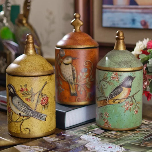 Three decorative jars with bird designs on a table.