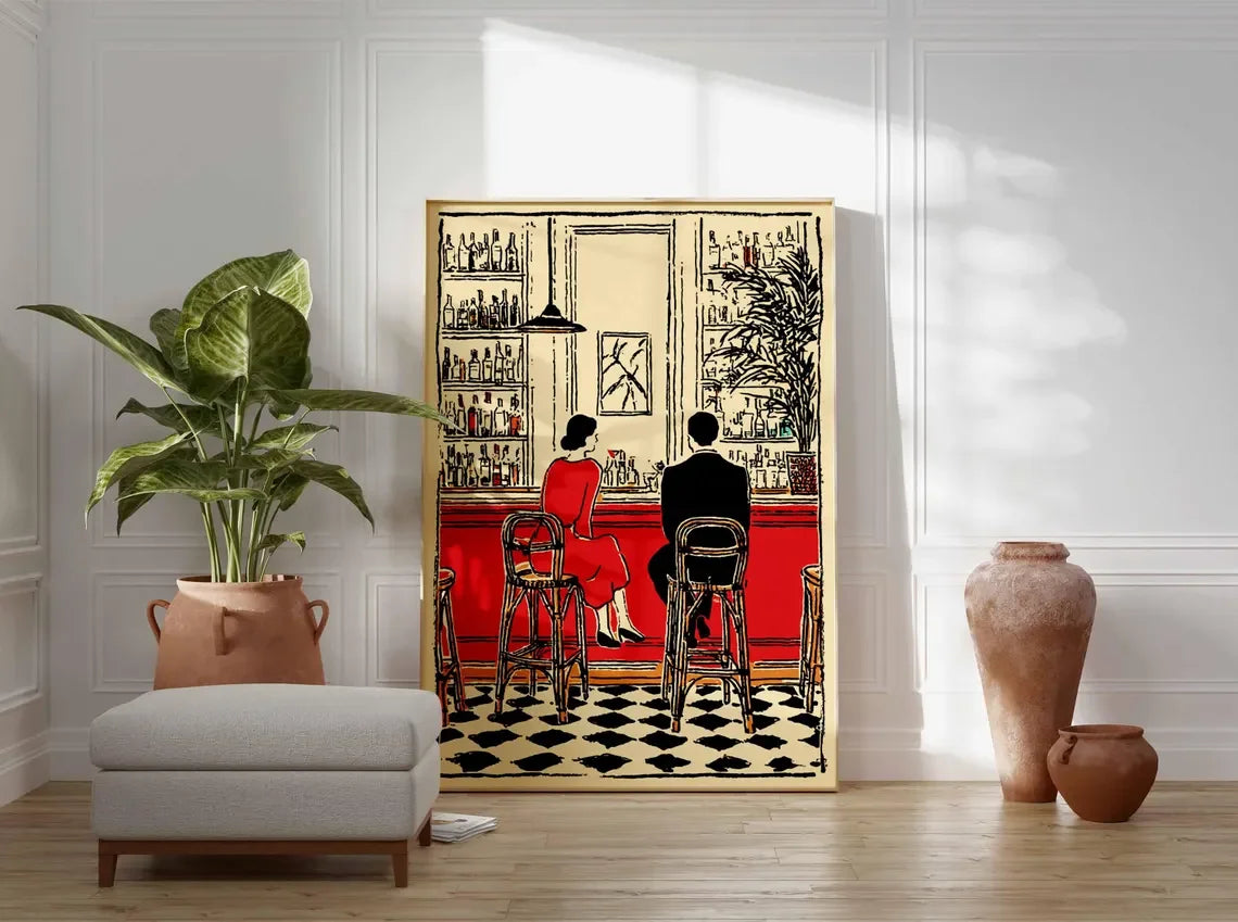 A framed art print depicting a vintage bar scene with a woman in a red dress and a man from behind, styled in a bright room with a potted plant, ottoman, and terracotta vases.