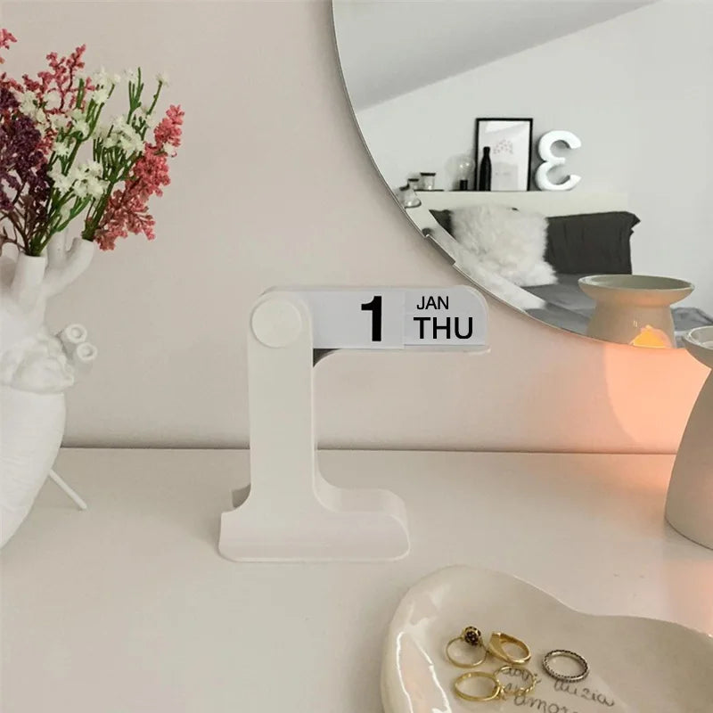 White desk organizer with a calendar displaying '1 Jan Thu' on a desk with flowers and jewelry.