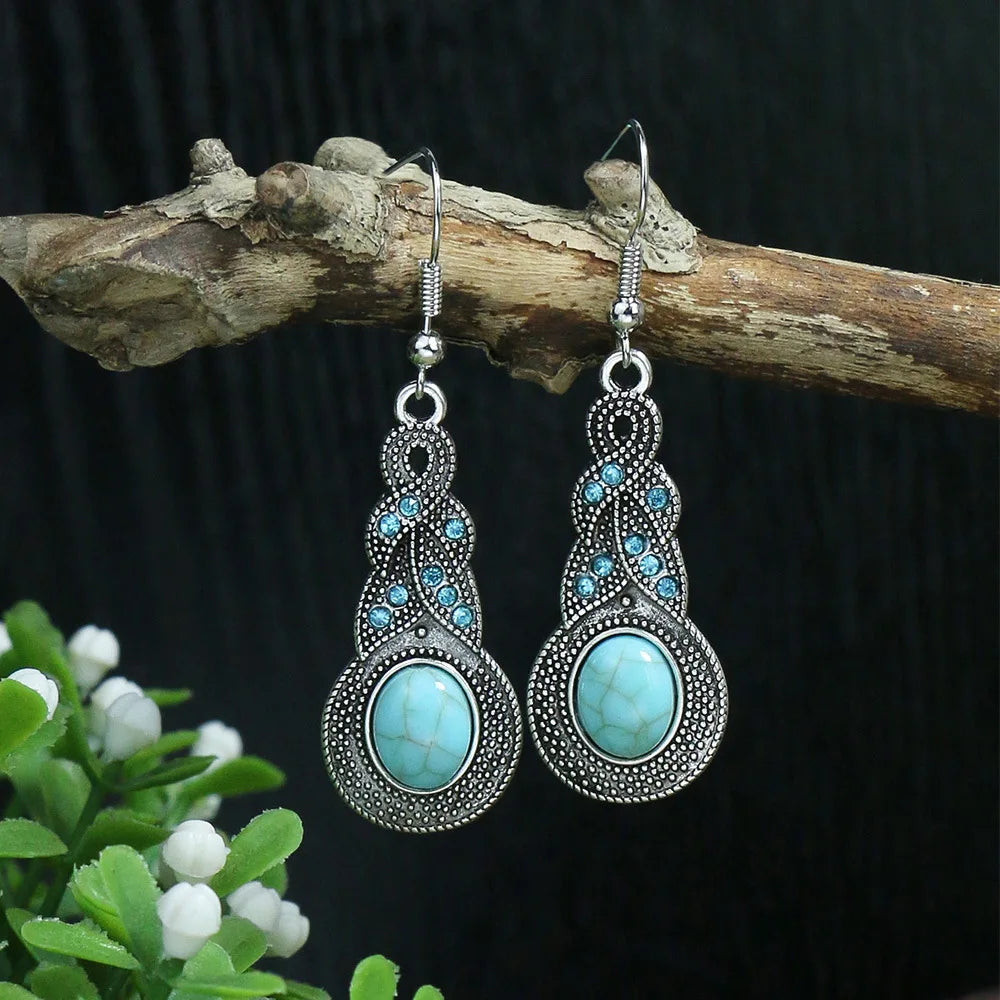 Turquoise earrings with silver detailing on a branch against a dark background