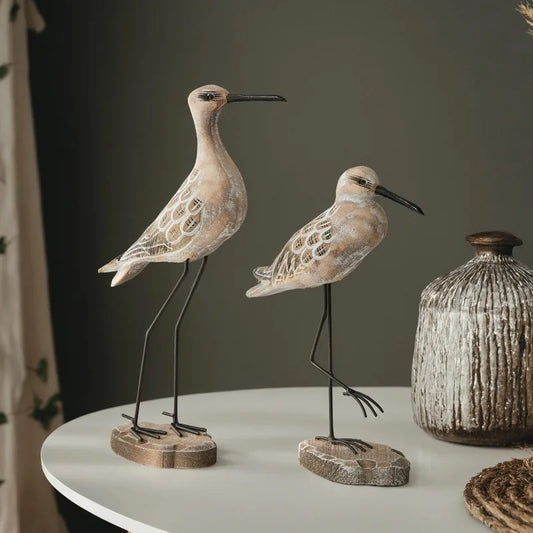 Two decorative bird figures on a table with a vase in the background.