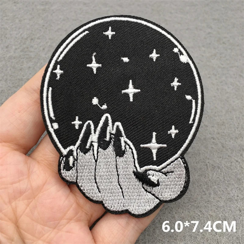 Embroidered patch with hands holding a crystal ball and stars on a gray background