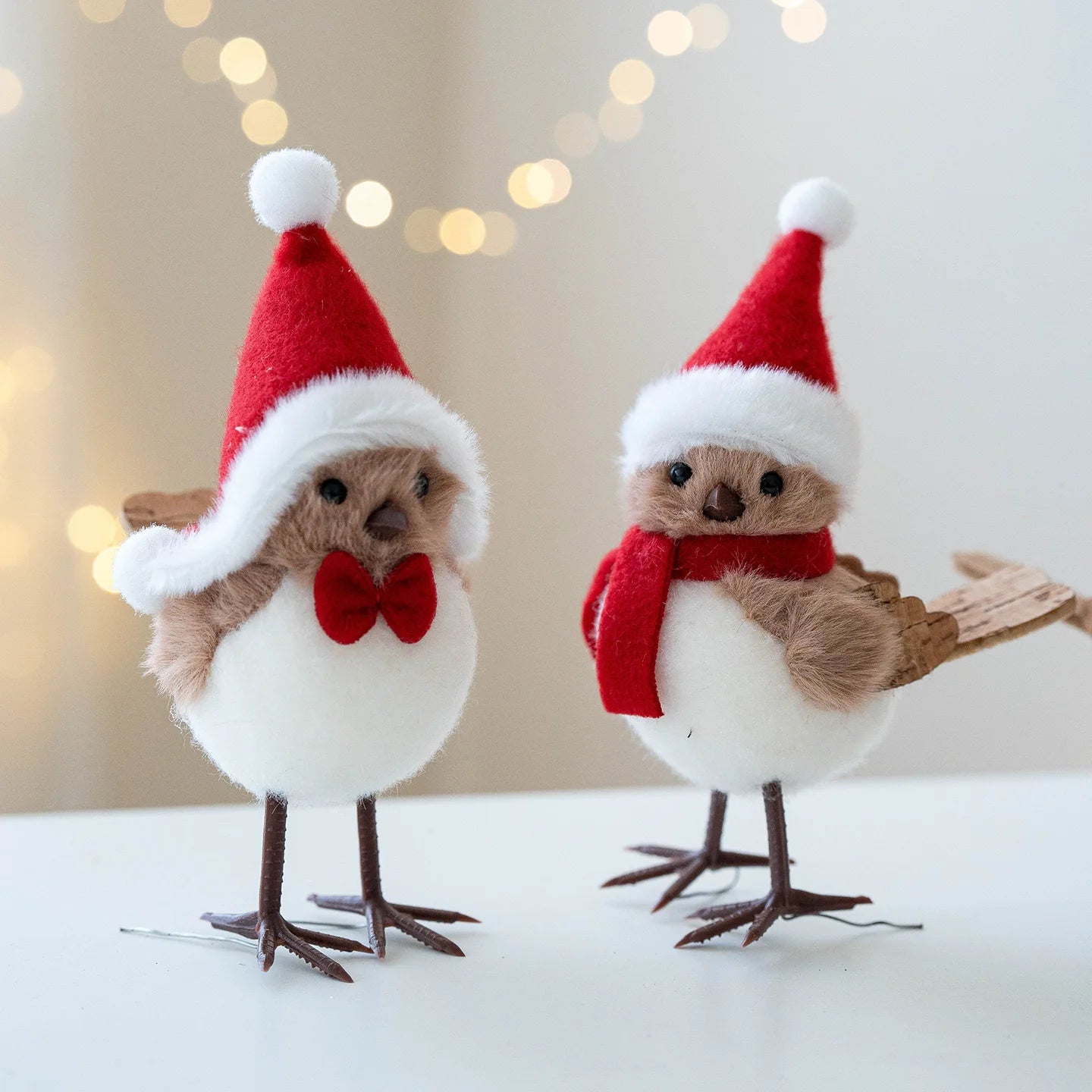 Two decorative birds wearing Santa hats and scarves on a light background with blurred lights.