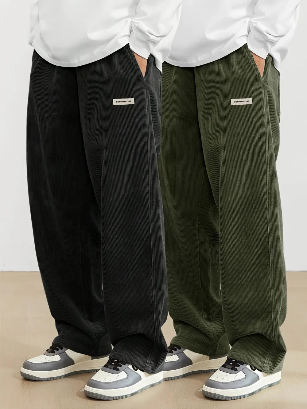 Two people wearing black and green corduroy pants with white shirts and sneakers on a plain background.
