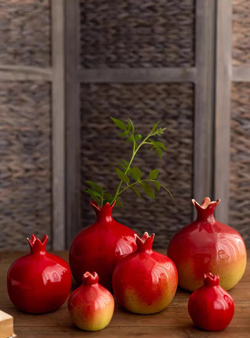 Red ceramic pomegranate decorations on a wooden surface with a textured wall background.