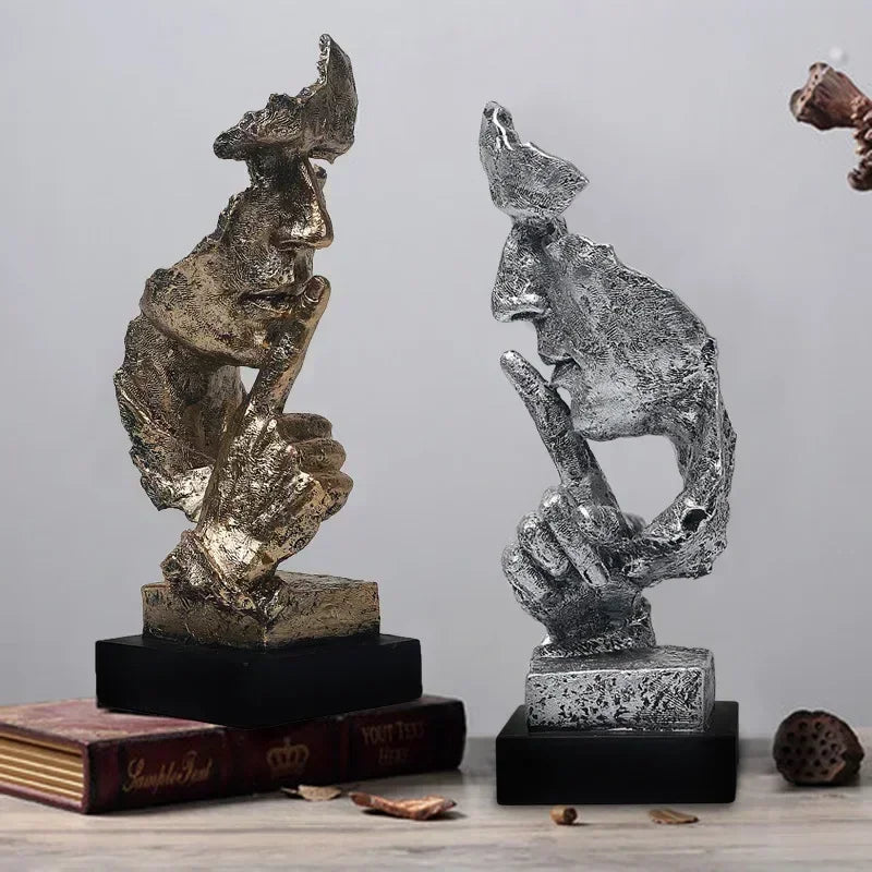 Two Art Deco-style bronze "Dont' Speak" sculptures in bronze and silver on a wooden table and grey background