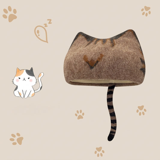 A cat-shaped wool hat in brown and black tiger-stripe pattern, shown on a beige background with paw prints, a sleeping cat illustration.