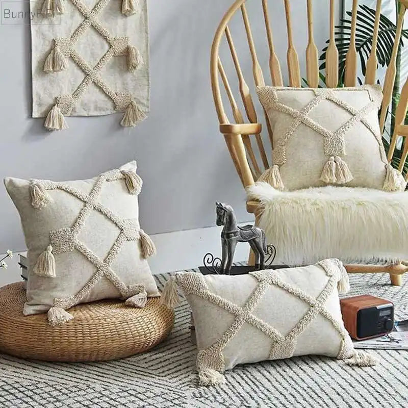 Boho Decorative pillows with tassels on a chair and ottoman in a room with a textured rug and wall art.
