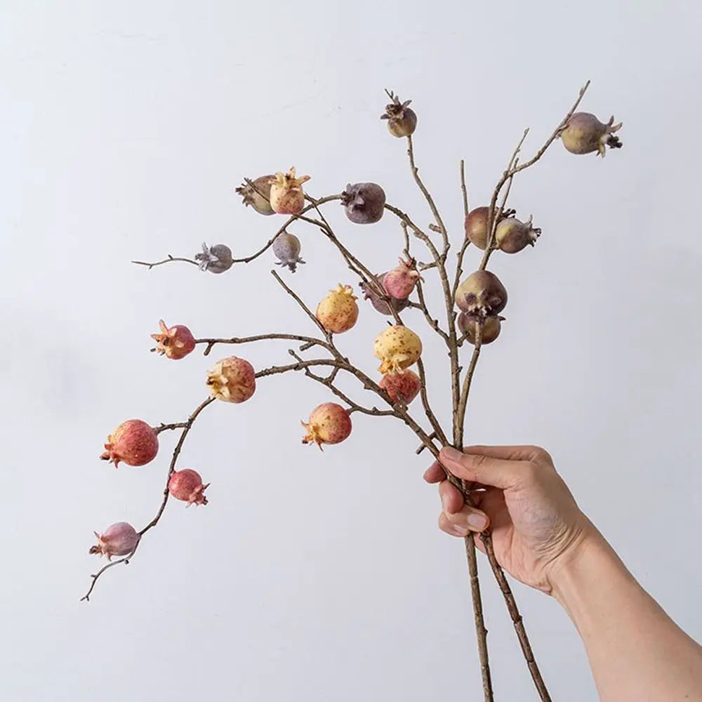Hand holding dried floral branches with pods against a light background