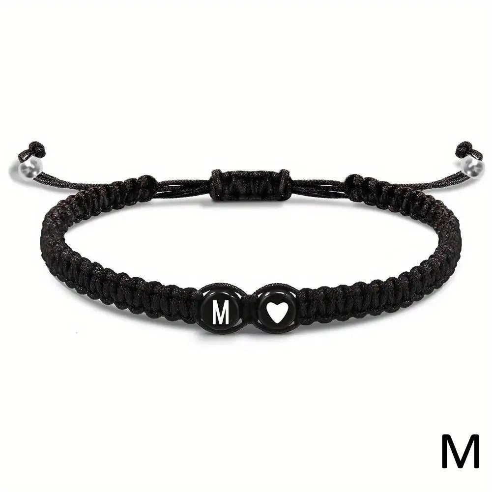 Black braided bracelet with heart and letter 'M' charm on a white background