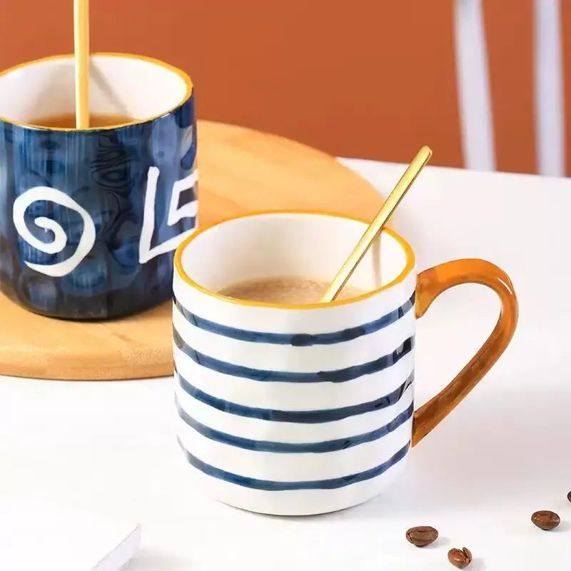 Striped mug with a gold spoon being filled with coffee next to a blue mug.