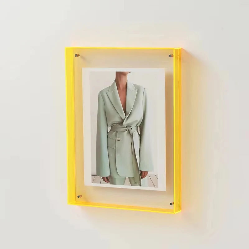 Yellow frame with a photo of a person wearing a light green coat on a white wall.