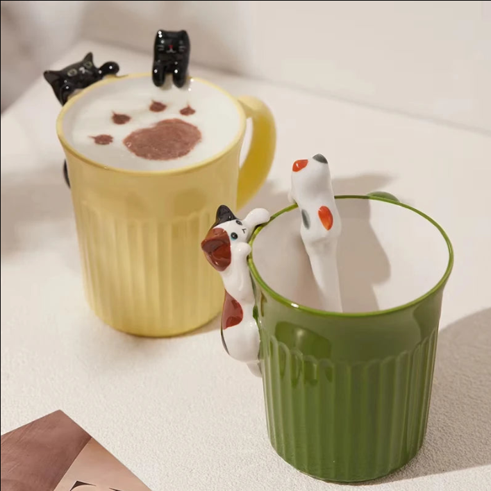 Green and yellow ceramic cat mugs with a 3D cat climbing over the rim.