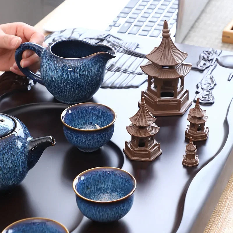Blue ceramic teapot and cups with miniature pagoda structures on a desk.