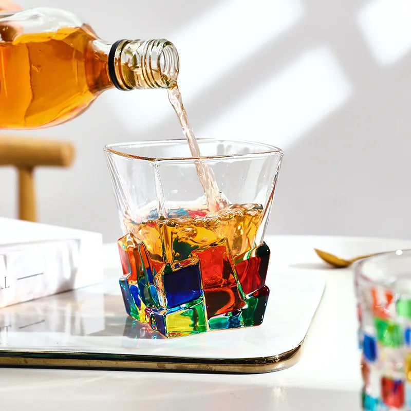 Collection of colourful glass tumblers with vibrant red, blue, green and orange geometric detailing displayed together in natural light.