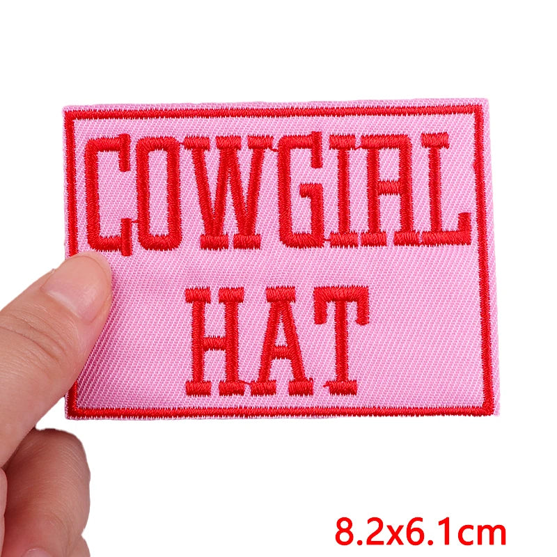 Pink patch with red text 'COWGIAL HAT' held by a hand on a white background