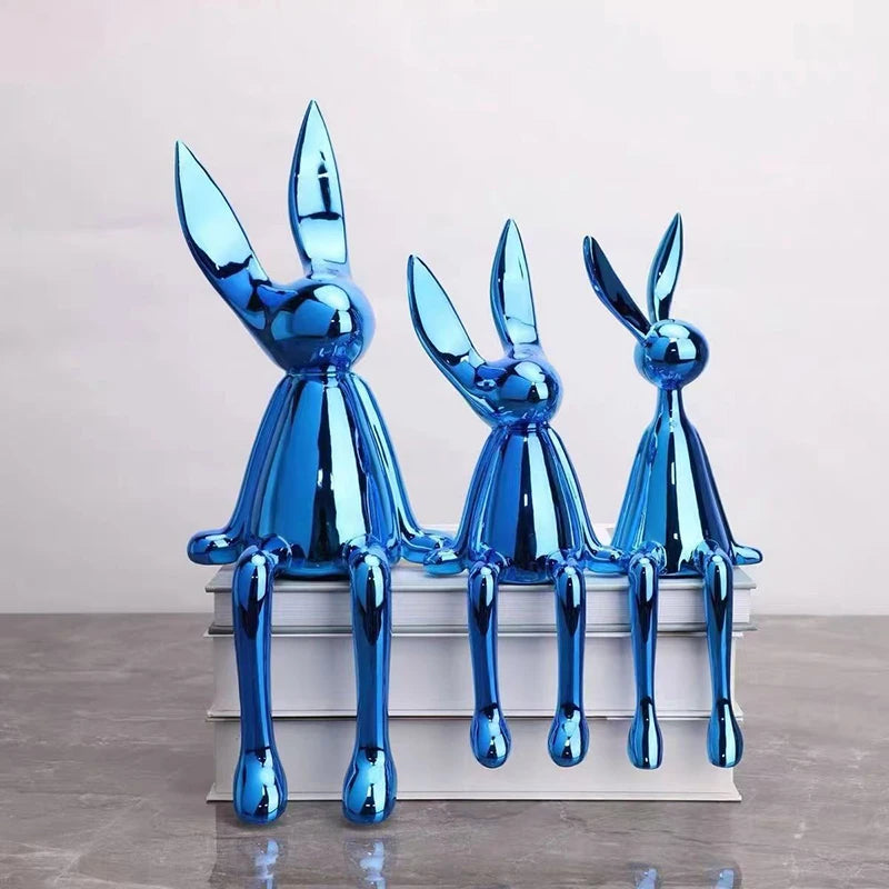 Three blue rabbit sculptures on a white platform against a light gray background