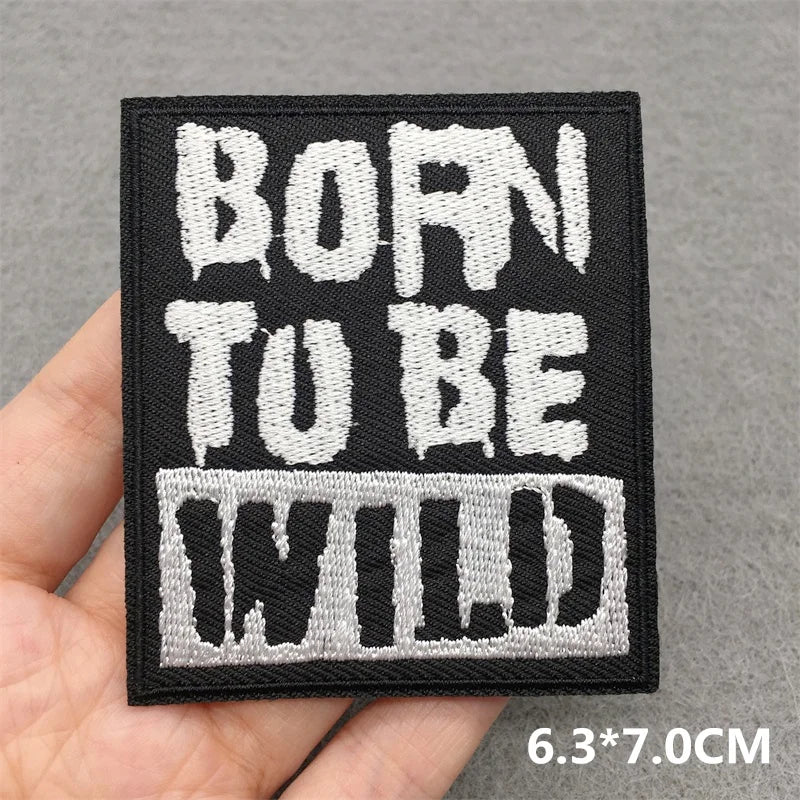 Embroidered patch with 'Born to be Wild' text held in a hand against a gray background