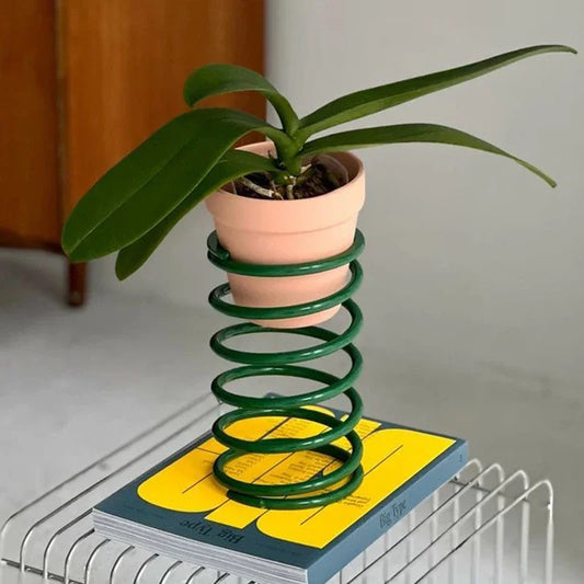 Potted plant on a book with a green spring stand against a neutral background