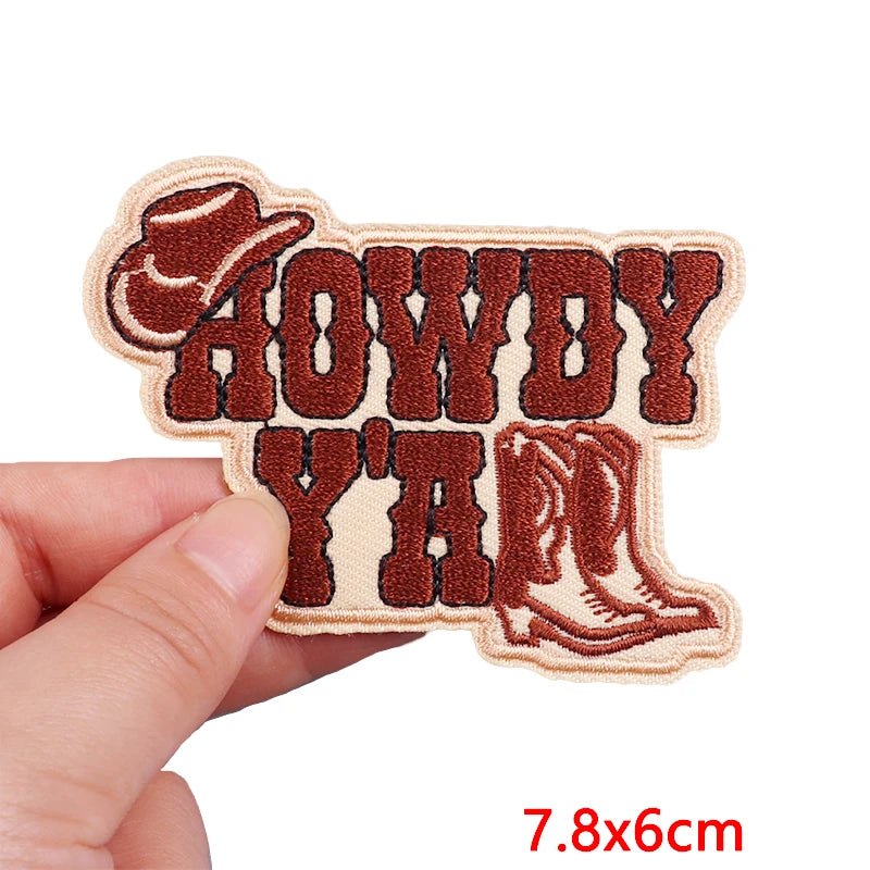 Embroidered patch with 'Howdy Y'all' text held by a hand, on a white background.