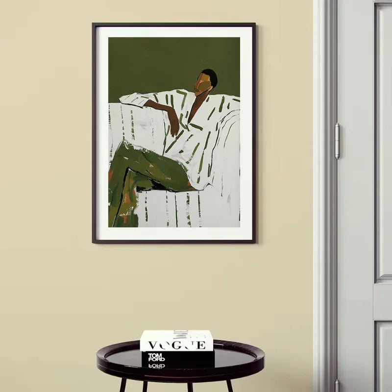 Framed artwork of a person sitting on a wall with a magazine on a table below.