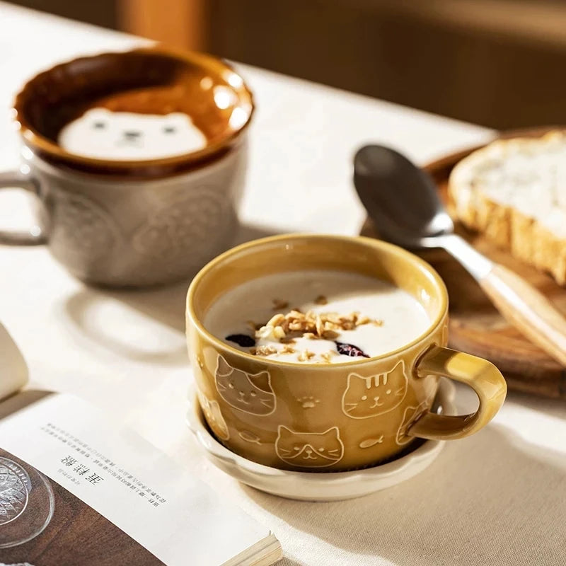 Cup of cereal with cat design on a table with a bowl and spoon.