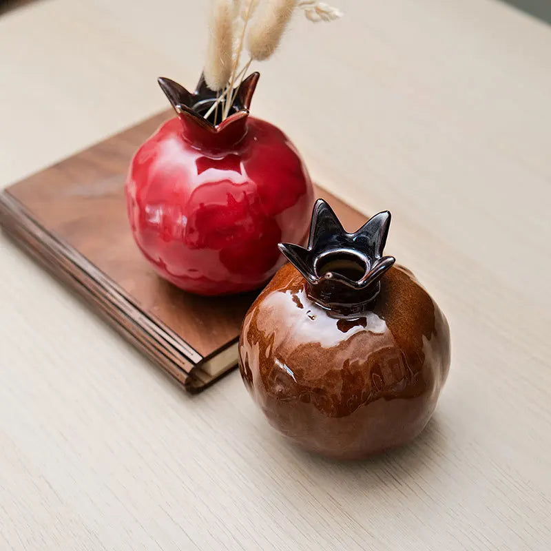 Two ceramic pomegranate, one red and one brown, on a light wooden surface.