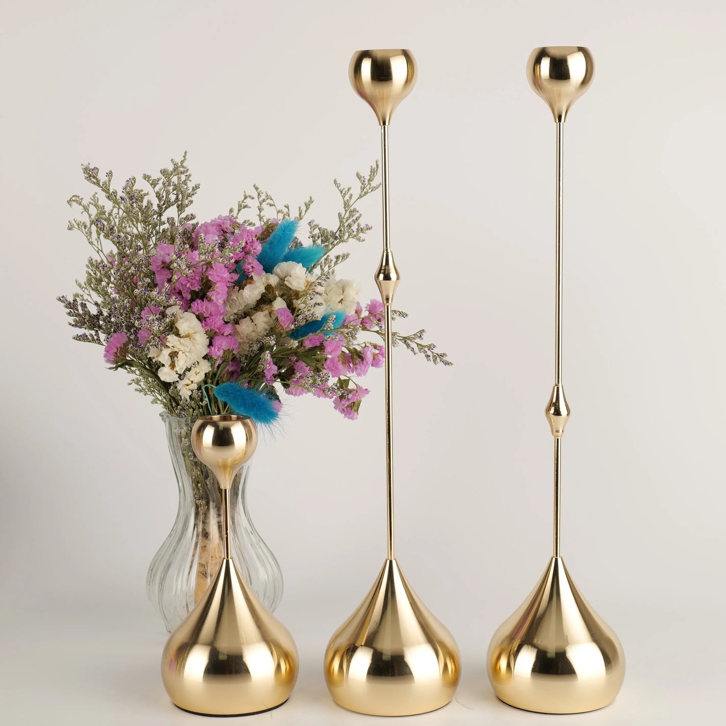 Set of three gold vases with a small vase containing flowers on a light background