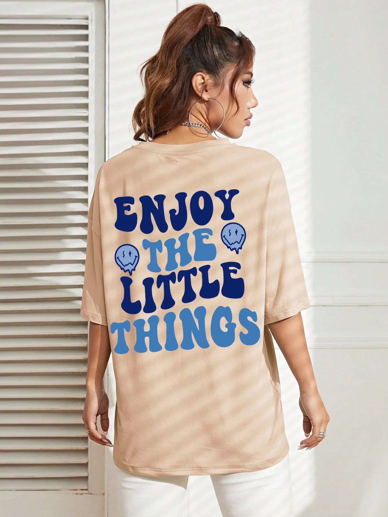 Woman wearing a beige t-shirt with 'ENJOY THE LITTLE THINGS' text in blue.